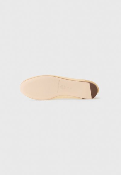 Beige suede shoe sole with a smooth finish, featuring a textured brown heel cap and subtle embossed branding on the insole.