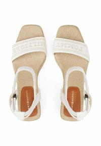 Beige Stoff Wedge Sandalen mit weißen Riemen, die das "Tommy Hilfiger" Logo zeigen. Offenes Futter-Design und strukturiertes Material. Quadratische Zehenform.