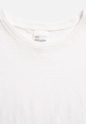 Primo piano di una T-shirt bianca a girocollo con un'etichetta visibile con la scritta "NJCo" e un messaggio sulla responsabilità del prodotto e dei lavoratori.