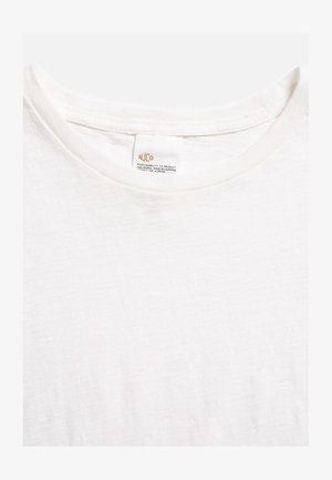 Primo piano di una T-shirt bianca a girocollo con un'etichetta visibile con la scritta "NJCo" e un messaggio sulla responsabilità del prodotto e dei lavoratori.