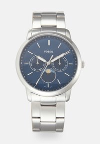 Montre en acier inoxydable avec un cadran bleu, des index argentés et trois sous-cadrans pour le jour, la date et la phase lunaire. Bracelet en métal brossé.