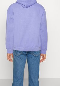 Felpa con cappuccio lilla realizzata in tessuto morbido, con vestibilità comoda e polsini a coste. Abbinata a jeans blu in denim, con tasche posteriori.