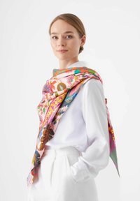 Zijde sjaal met een levendig bloemenpatroon in roze, oranje en groene tinten, stijlvol gedrapeerd over een witte blouse.