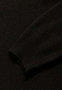 Zwarte gebreide pullover met mouwen, featuring een geribde manchette en zachte textuur, die een naadloos ontwerp en een gelijkmatige kleuring door het geheel benadrukt.