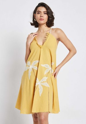 Gelbes Halfterkleid mit tiefem V-Ausschnitt, fransigen Kanten und weißem, gesticktem Blätterdesign, aus leichtem Stoff gefertigt.