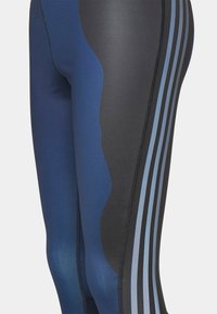 Leggings navy e neri con accenti blu, caratterizzati da una texture liscia, pannelli a contrasto e tre strisce verticali lungo un lato.
