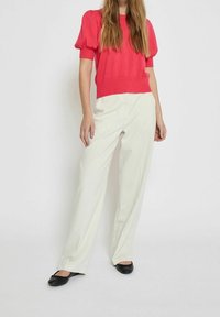 Červený pletený top s krátkým rukávem a nafouknutými rukávy, spárovaný s bílými kalhotami s vysokým pasem a širokými nohavicemi a černými plochými botami. Hladká textura.