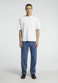 Vit bomullströja med rund halsringning, parat med blå jeans i avslappnad passform. Svarta skor med glansig yta fulländar outfiten.
