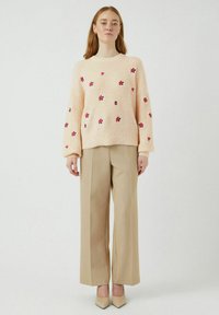 Svijetloružičasti pleteni pulover s cvjetnim vezom u crvenoj i tamnoružičastoj boji. Uparen s bež širokim hlačama i be�ž cipelama s uskim vrhom.