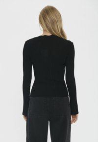 Fekete bordázott hosszú ujjú felső, testhez simuló szabással, magas nyakkal és varrás nélküli hátrésszel. Sötét, magas derekú farmernadrággal, zsebekkel párosítva.