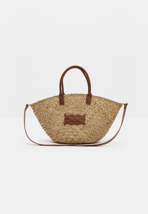 Sac à main en paille tissée avec des anses et des garnitures en cuir marron, doté d'une base ronde et d'une bandoulière amovible.