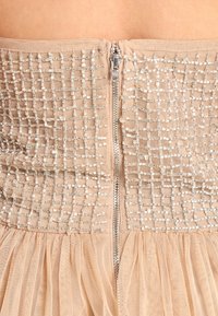 Beadad utan axelbands topp i beige med texturerad tyg, en bakre dragkedja och en tylskjol; har glittrande accenter och en åtsittande liv.