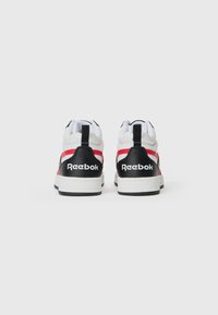Balts, melns un sarkans Reebok sporta apavu pāris redzams no aizmugures uz vienkārša balta fona.