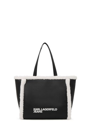 Črna torba z belim umetnim krznom na robovih in belim logotipom "KARL LAGERFELD JEANS" na sprednji strani, opremljena z dvema črnima naramnicama.