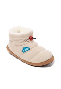Zapatilla de pana beige con un forro de felpa blanca, punta redonda, suela marrón y detalles rojos. Presenta un logotipo en el lateral y un puño plegable.