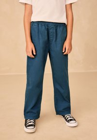 Zelenomodré nohavice s elastickým pásom, voľným strihom a bočnými vreckami, kombinované s čiernymi teniskami s bielymi šnúrkami a gumovou podrážkou.