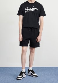 Černé bavlněné tričko s bílým logem "Jordan", doplněné černými kraťasy s tkaničkou. Celý outfit doplňují černé a bílé sportovní boty.