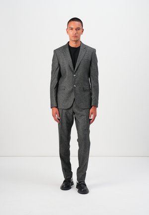 Grey textured suit with a two-button blazer and matching trousers. Worn over a black shirt, paired with black shoes.