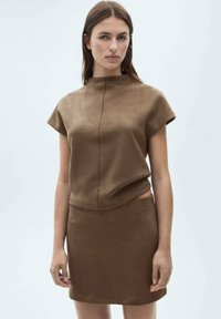 Un top din suede maro cu mâneci scurte și guler înalt, asociat cu o fustă mini maro asortată, ce prezintă o textură netedă și un design ajustat.
