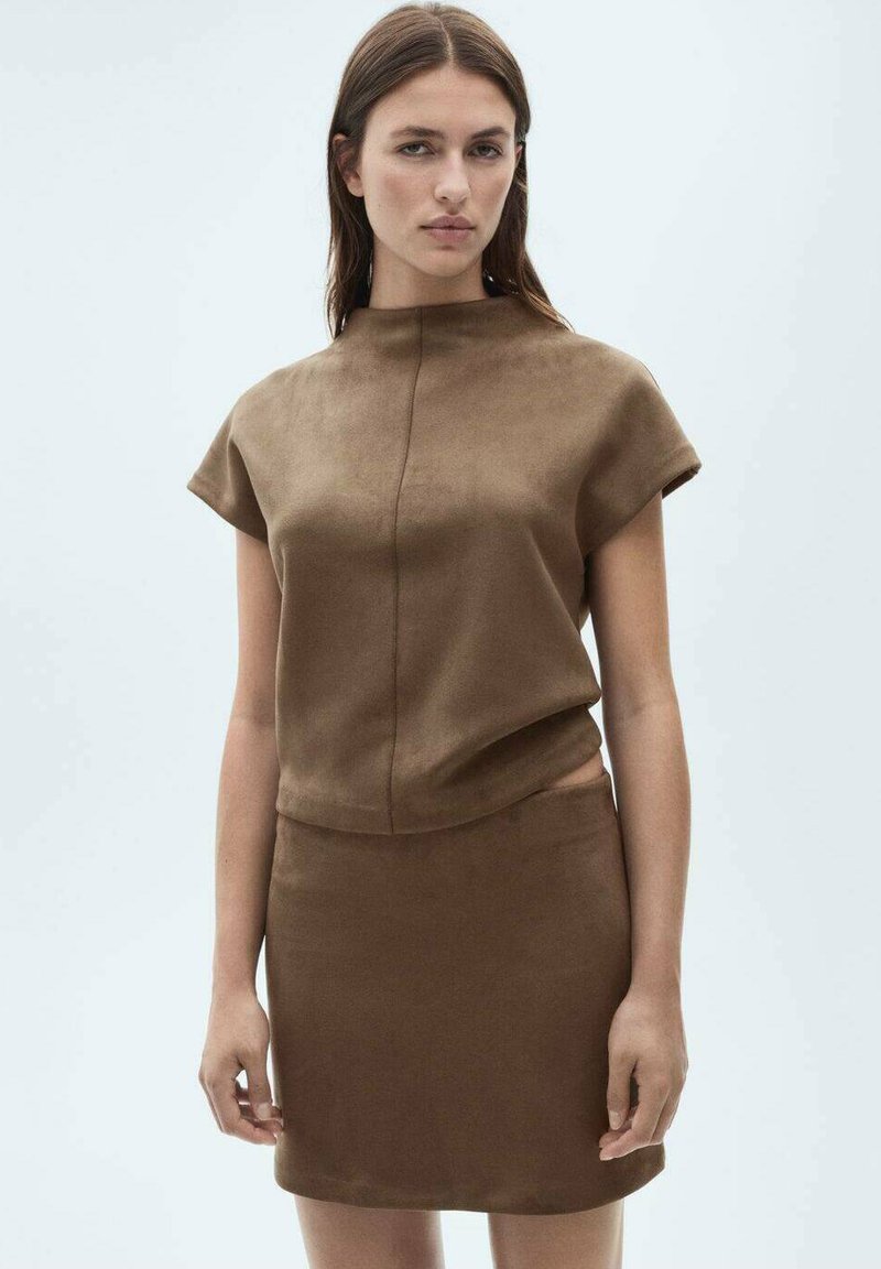 Un top din suede maro cu mâneci scurte și guler înalt, asociat cu o fustă mini maro asortată, ce prezintă o textură netedă și un design ajustat.