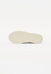Suola della scarpa con una superficie texturizzata, di colore beige chiaro e forma arrotondata. Nessun marchio o elemento decorativo visibile.