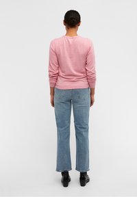 Ljusrosa långärmad skjorta med ribbade ärmmuddar, tillsammans med ljusblå vida jeans och svarta klumpiga skor, sedd bakifrån.