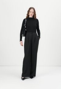 Cămașă neagră cu dungi, mânecă lungă, pantaloni negri largi și pantofi cu vârf ascuțit negri. Modelul ține o geantă neagră de umăr. Texturi netede, croială ajustată.