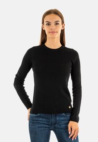 Pull noir à manches longues en tricot, doté d'un col rond et d'un petit logo sur le bas à gauche.