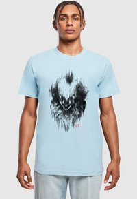 Lyseblå t-shirt med korte ærmer, der har et sort grafisk design, der ligner et klovnehoved med lydwave-mønstre og røde accenter.