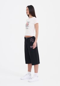 Camiseta corta de color rosa claro con un estampado gráfico, combinada con pantalones cortos negros hasta la rodilla con detalles en colores y zapatillas blancas.