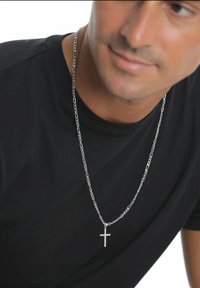 Silverkedja med ett litet korshänge, bärs över en svart skjorta. Kedjan har sammanlänkade länkar och en blank yta.