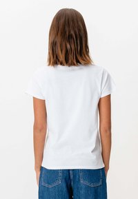 Hvid bomulds t-shirt med korte ærmer og rund hals, vist fra bagsiden. Sammen med blå denim jeans. Glat tekstur, afslappet design.