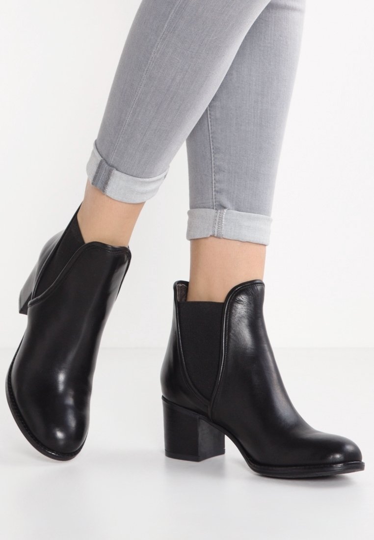 Bottes chevilles en cuir noir avec un bout arrondi, des panneaux latéraux élastiques et un talon bloc. Texture lisse avec un design minimaliste.