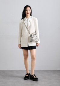 Hvid dobbeltradet blazer med tekstureret finish, kombineret med en hvid bluse med sløjfe. Sort plisseret nederdel og platformsko. Taske med slangeprint.