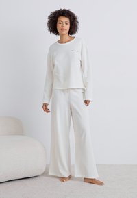 Conjunto de roupa de lazer branco com uma blusa de manga longa canelada e calças largas. Textura suave com um detalhe de costura simples. Tecido leve.