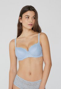 Sujetador de encaje azul claro con copas lisas, bordes festonados y tirantes ajustables. Combinado con unas braguitas de encaje a juego, que presentan un patrón floral.