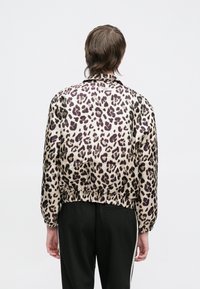 Žakete ar leopardu rakstu bēšā un violetā krāsā, ar elastīgām aprocēm un apakšmalu, ar gludu, spīdīgu tekstūru.