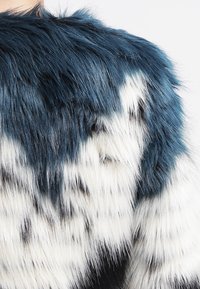 Umělé kožešinové oblečení s kombinací tmavě modrých a bílých textur a pruhovaným vzorem, měkkým povrchem a různými délkami vláken.