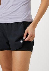 Lilla, tekstureeritud spordipealse koos mustade lühikeste pükstega, millel on F logo, rõhutades sileda kangast ja hästi istuvat disaini.