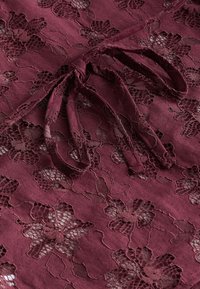 Tissu bordeaux avec motif en dentelle florale et détail d'un cordon de serrage noué assorti en couleur et texture.
