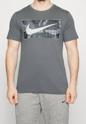 Gray short-sleeve T-shirt made of cotton, featuring a large white Nike logo graphic on the front against a black grid pattern.