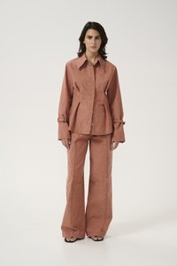 Rust-colored coordinated outfit featuring a collared button-up shirt with flared sleeves and high-waisted flared pants with visible stitching.