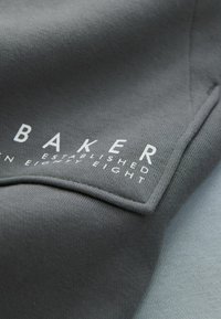Gray sweatshirt fabric with a smooth texture, featuring white lettering "BAKER ESTABLISHED EIGHTY EIGHT" on the front.