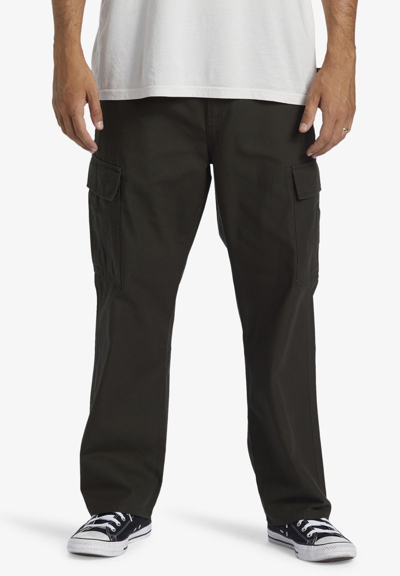Cargo pants in dark green, made of durable fabric. Features include side pockets, a straight-leg design, and a relaxed fit. Paired with black sneakers.