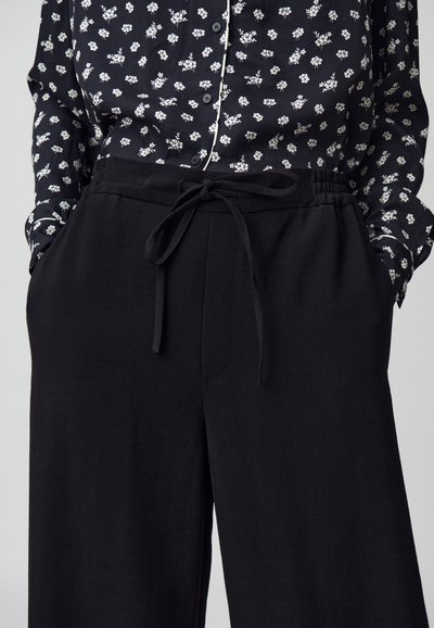 Pantaloni neri a gamba larga con una vita elastica e un laccio da annodare. Abbinati a una camicia a maniche lunghe a bottoni con motivo floreale in bianco e nero.