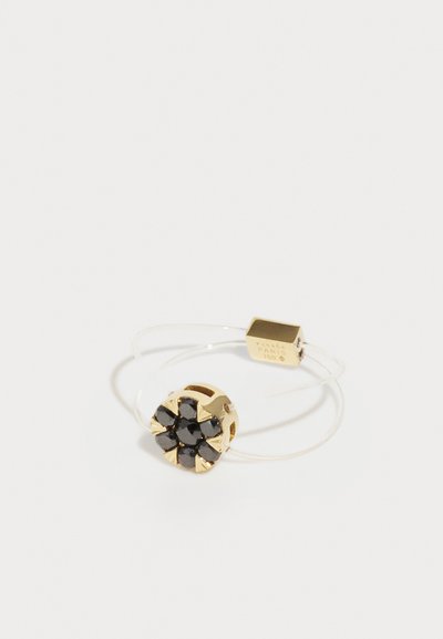 Anillo de oro con una banda elástica transparente y un conjunto redondo de piedras negras en un diseño floral; cuenta con una pequeña etiqueta de oro con "París" y "750."
