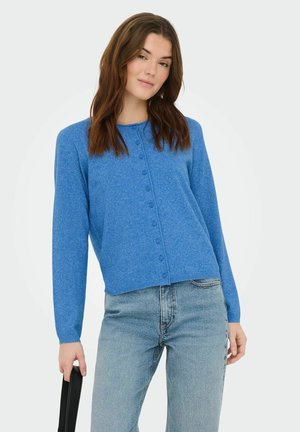 Cardigan boutonné bleu en tissu tricoté doux, avec un col rond et des manches longues, accompagné d'un jean en denim clair.