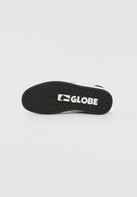 Black rubber shoe sole with textured grip patterns and a white "GLOBE" logo. Features a rounded shape with a smooth edge.