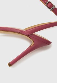 Ροζ δερμάτινο πέδιλο με ψηλό λεπτό τακούνι, λεπτό  σχεδιασμό με λουράκια, μυτερή μύτη και λεπτό τακούνι. Διαθέτει ασημί αγκράφα ως διακοσμητικό στοιχείο.