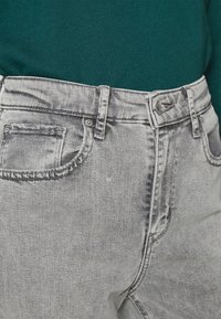 Jeans de mezclilla gris de talle alto con un acabado desgastado, que presentan un diseño clásico de cinco bolsillos y cierre de botón metálico. La textura parece suave.
